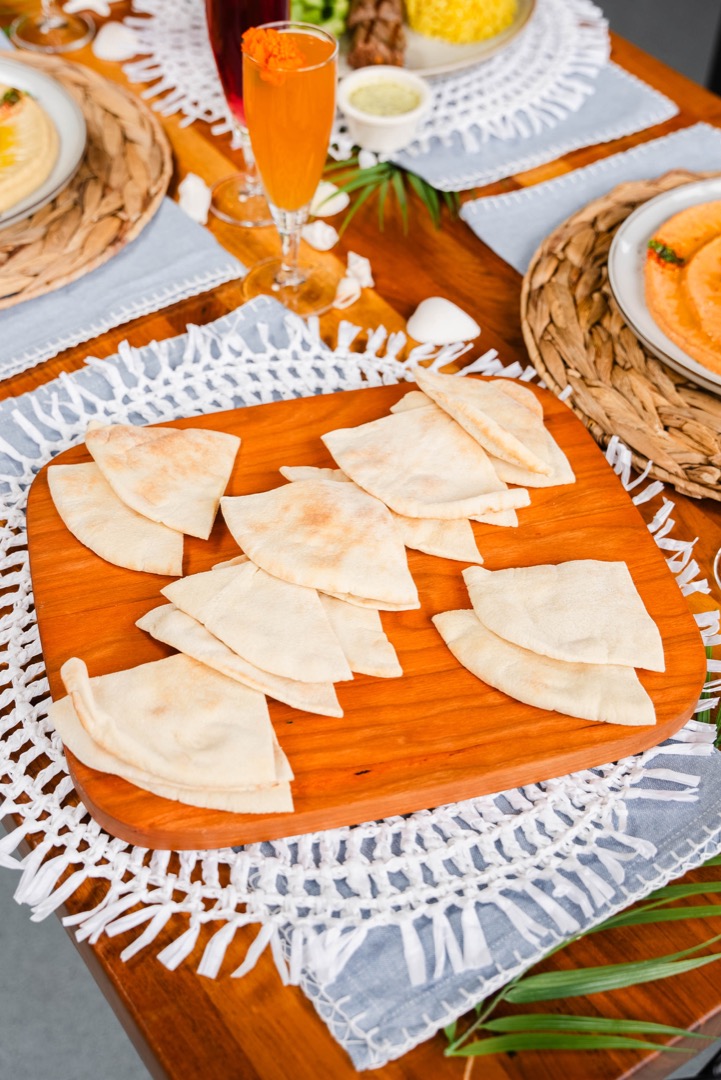 A serving of freshly baked pita bread cut into triangular slices, beautifully presented on a wooden board at a brunch table.