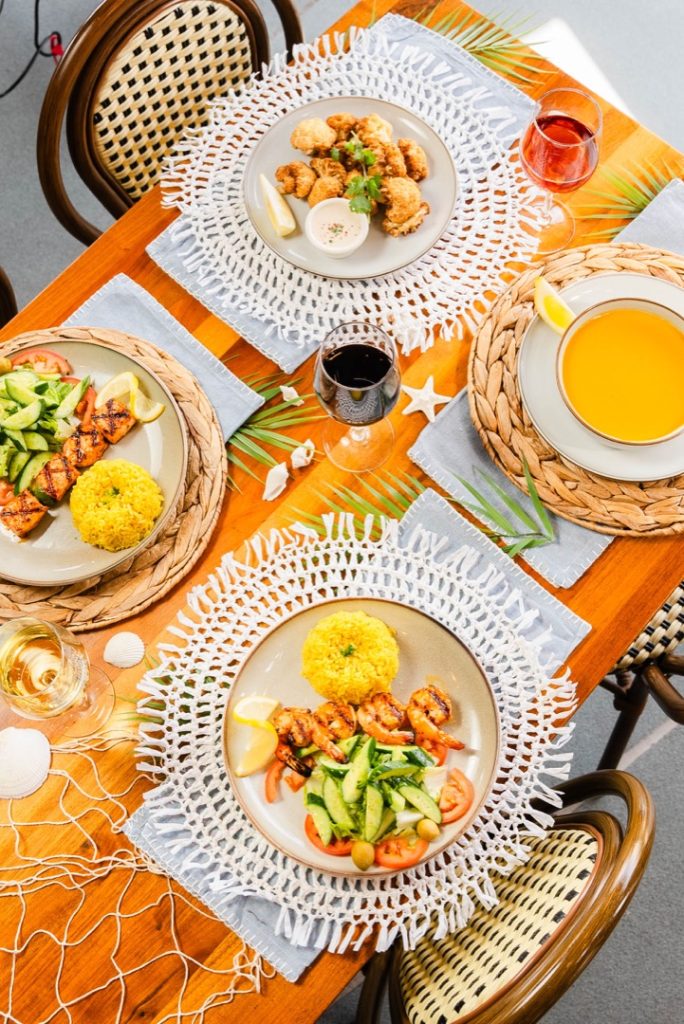 A table set with multiple Mediterranean-style dishes, including grilled shrimp, chicken skewers, fried cauliflower, and a bowl of soup.