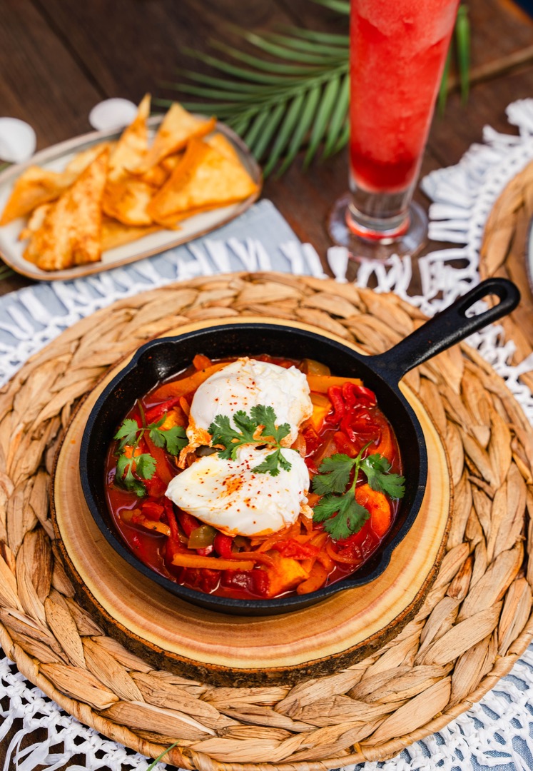 A cast iron skillet filled with shakshuka, a vibrant dish of poached eggs in a spiced tomato and bell pepper sauce, garnished with fresh cilantro.