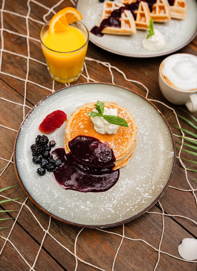 A breakfast plate with pancakes topped with whipped cream, berry compote, and a mint garnish, served with fresh berries.