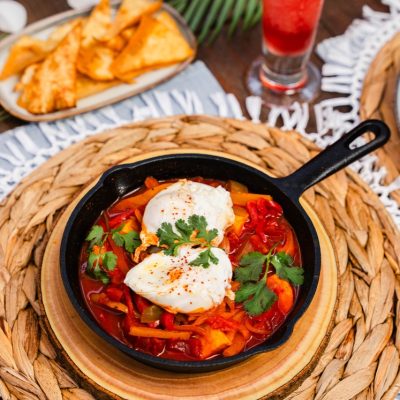 A cast iron skillet filled with shakshuka, a vibrant dish of poached eggs in a spiced tomato and bell pepper sauce, garnished with fresh cilantro.