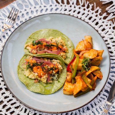 Two spinach breakfast tacos filled with scrambled eggs, avocado, and vegetables served with roasted breakfast potatoes.