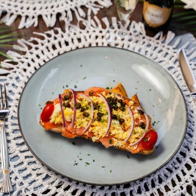 Smoked salmon toast topped with capers, red onion slices, and cherry tomatoes, garnished with herbs.